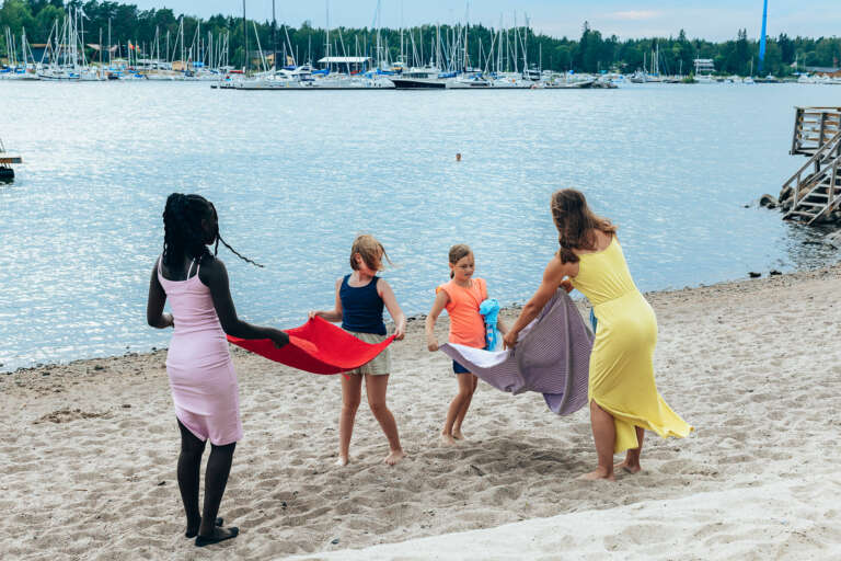 tre flickor och en kvinna står på stranden och viker handdukar