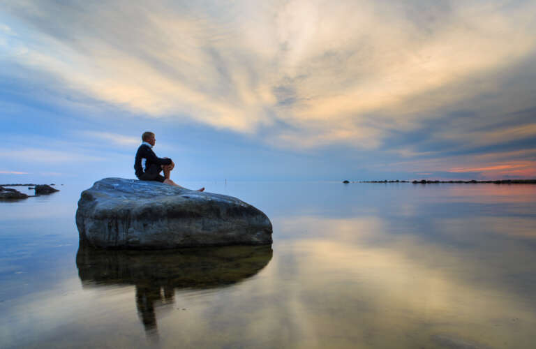 Henkilö istuu kivellä saaristossa ja katsoo horisonttiin