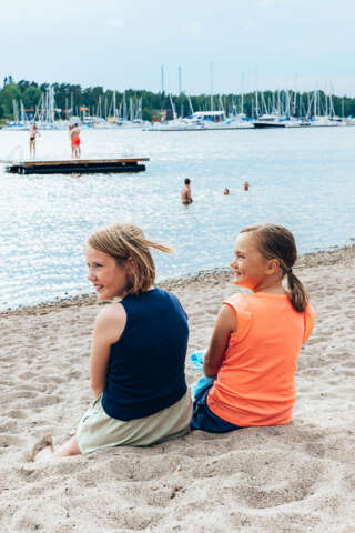 Två flickor sitter på stranden och ler